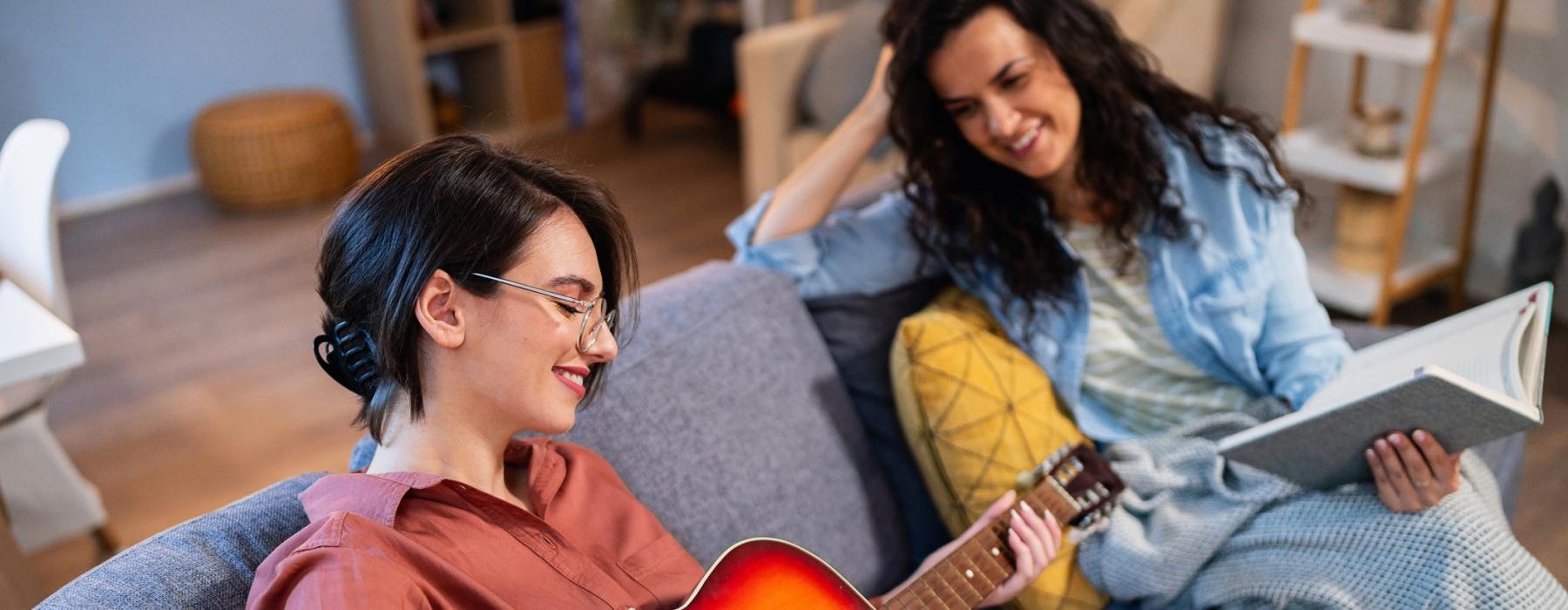a person playing a guitar next to a person sitting on a couch