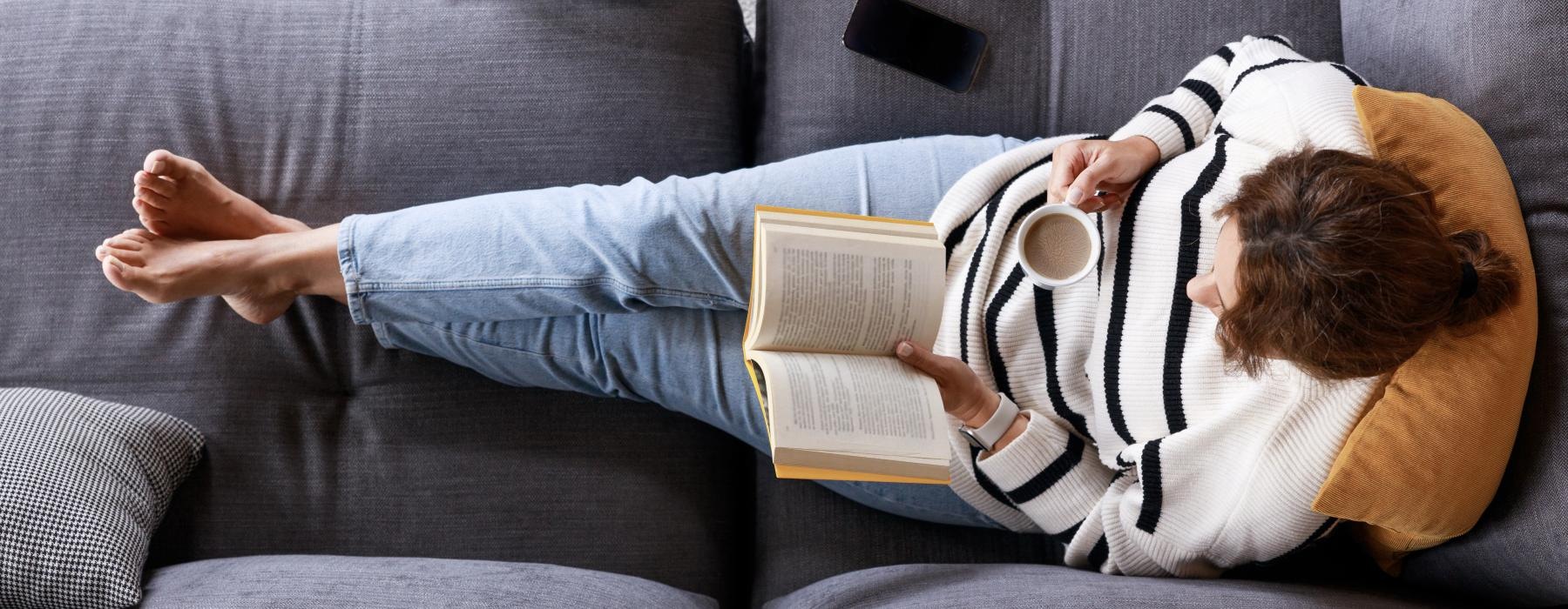 a person lying on a couch reading a book