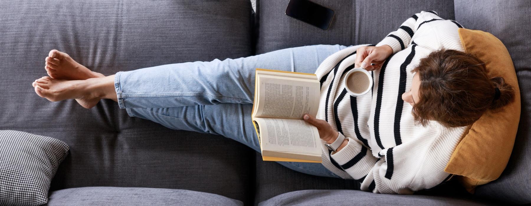 a person lying on a couch reading a book